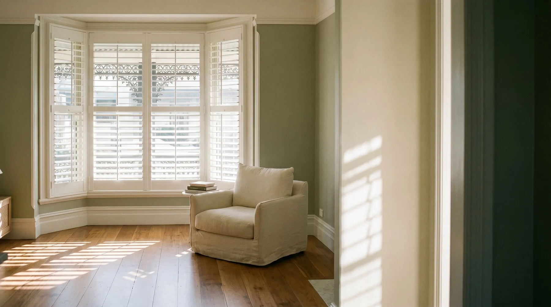 White plantation shutters across a terrace bay window, morning light striping the floorboards