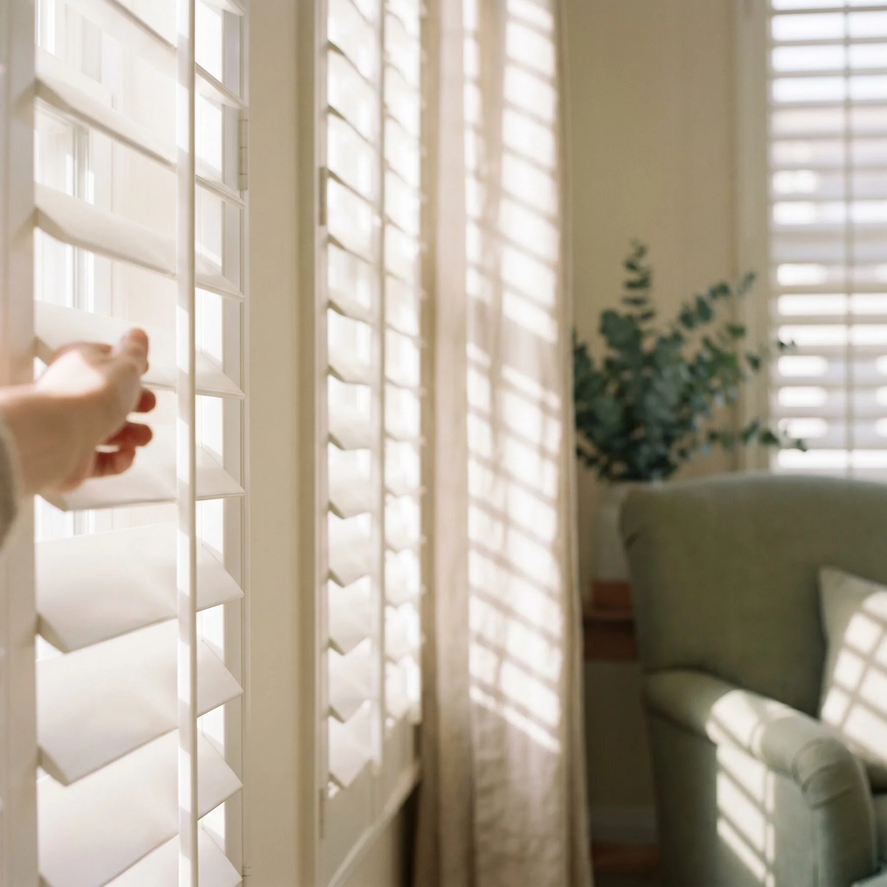 A hand tilting the louvre of a painted basswood shutter