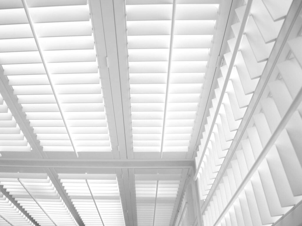 A low-angle, close-up view of several rows of white plantation shutters with their louvers partially open