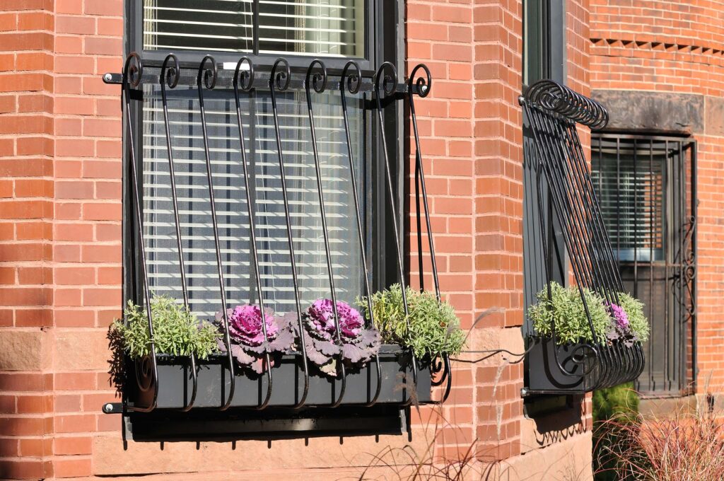 An eye-level view of two windows on a red brick building, protected by decorative black wrought iron security bars