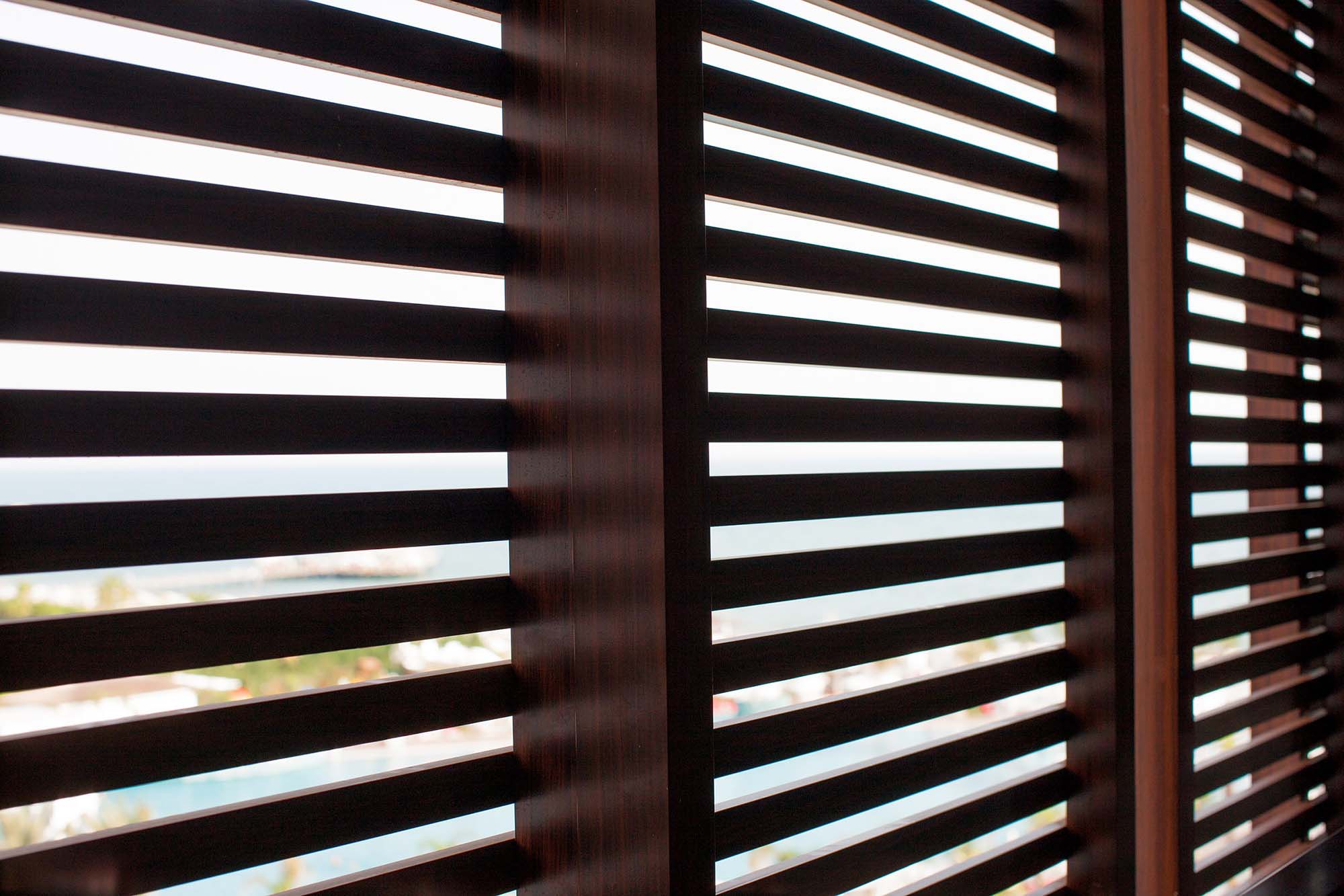 A close-up, interior view looking through dark wood horizontal louvers of a window