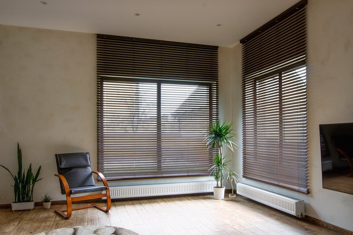 Blog » A modern, minimalist room with light wood floors featuring dark brown horizontal Venetian blinds on two large windows